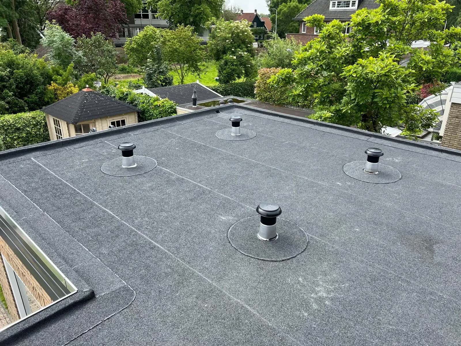 Plat dak met nieuwe donkergrijze dakbedekking en nieuwe ontluchtingen boven de tuin