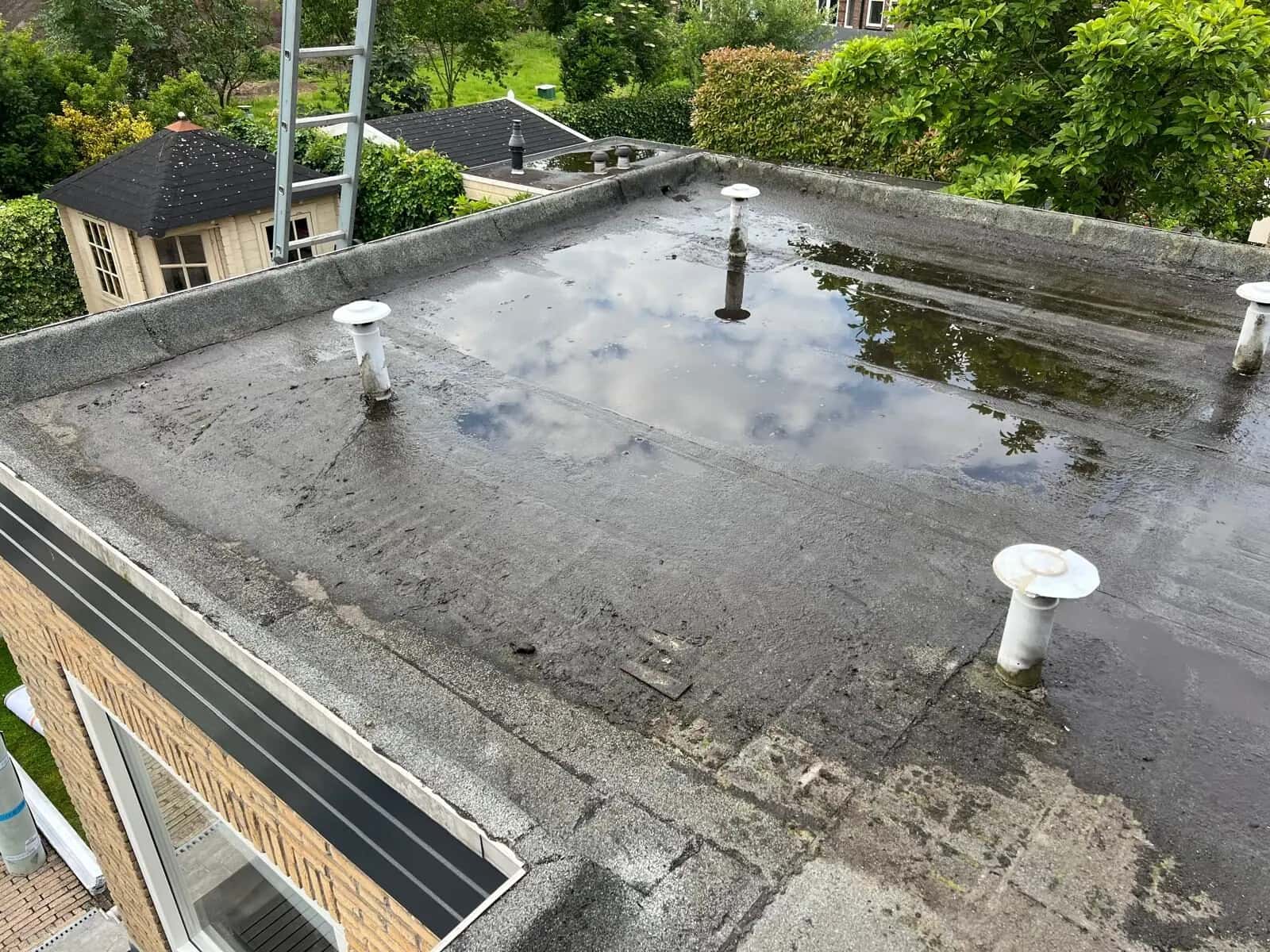 Plat dak met plassen staand water tussen witte ontluchtingen