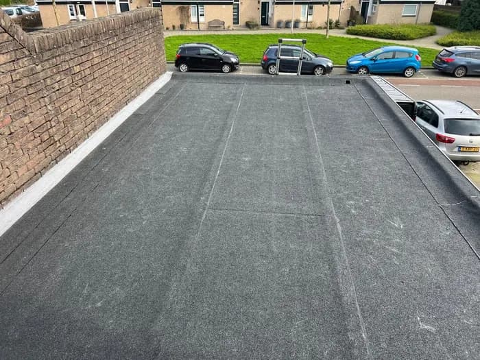 Nieuwe donkergrijze dakbedekking op een plat dak langs een bakstenen gevel