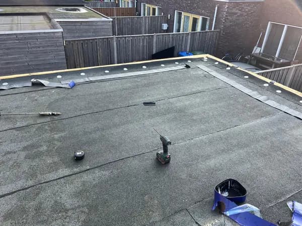 Vóór het werk: oude grijze dakbedekking met gereedschap en bevestigingsschijven langs de rand