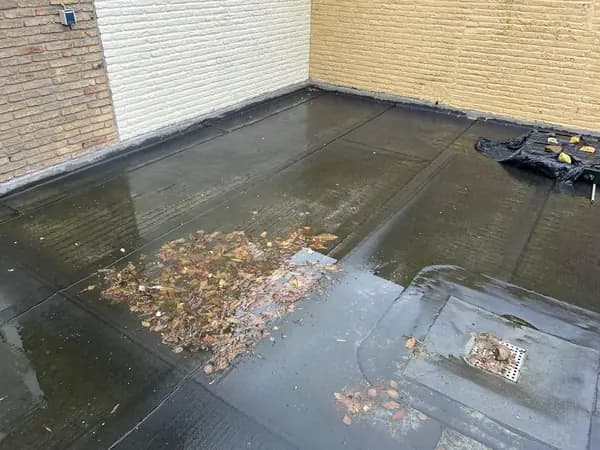 Vóór het werk: dakterras met plassen water, bladeren en een vervuilde dakafvoer