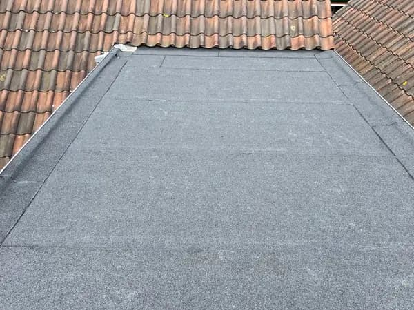 Na het werk: plat dak met nieuwe grijze dakbedekking tussen de pannendaken
