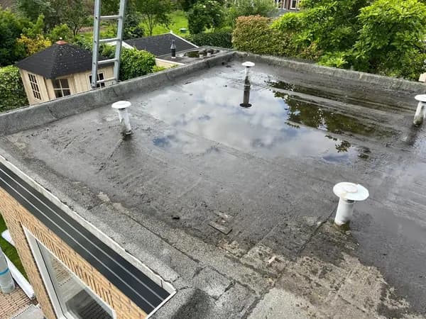 Vóór het werk: plat dak met grote plas staand water tussen witte ontluchtingen