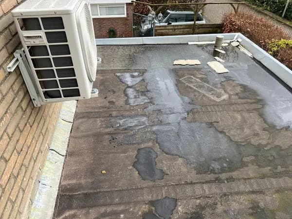 Vóór het werk: oude dakbedekking met natte plekken en vlekken naast een airco-unit