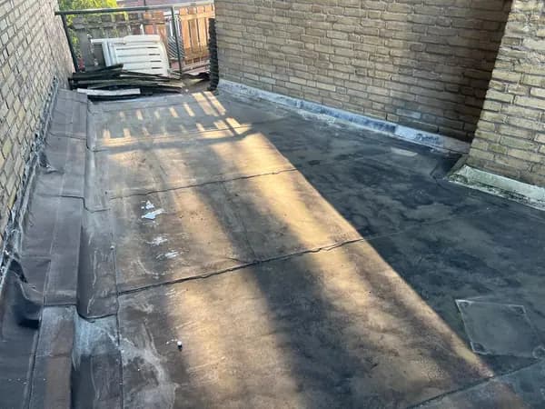 Vóór het werk: versleten bitumen dakbedekking op een dakterras tussen bakstenen muren, Dordrecht