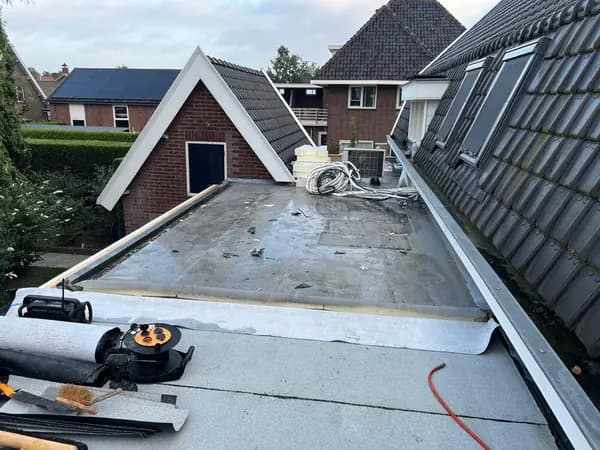 Vóór het werk: oud grijs plat dak tussen pannendaken met gereedschap op de voorgrond, Nieuwendijk