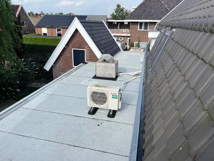 Afgewerkt plat dak met lichtgrijze dakbedekking en airco-unit tussen pannendaken