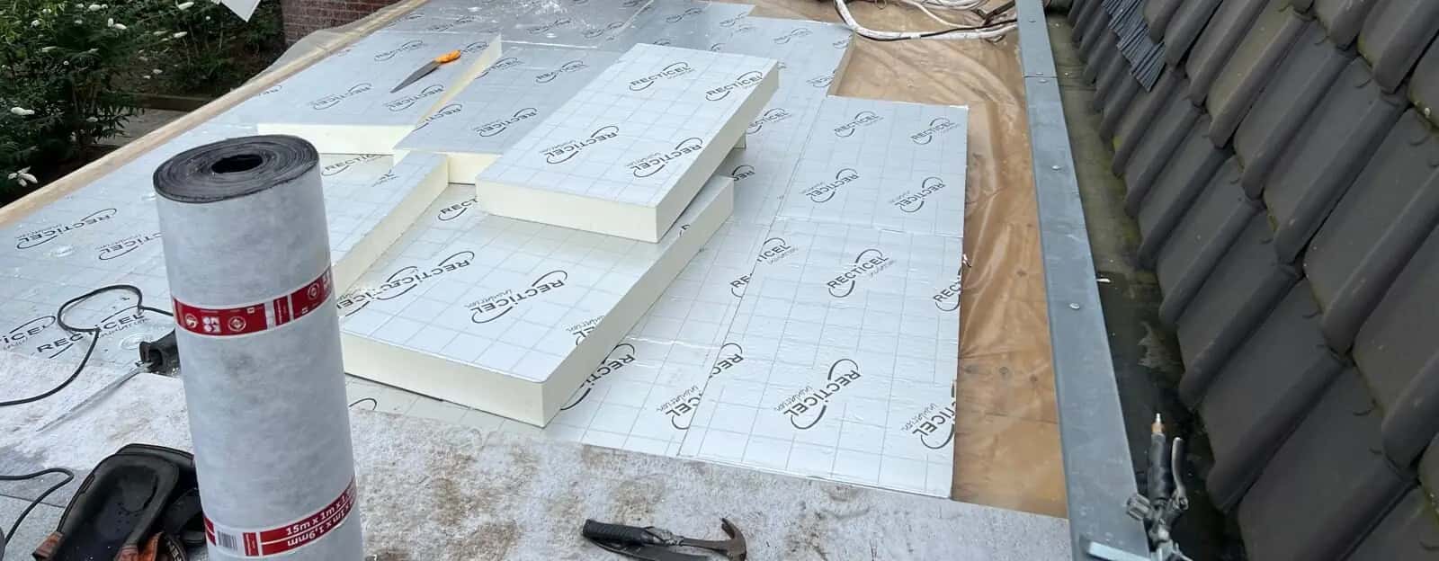 Isolatieplaten en een rol dampremmende laag op een plat dak naast een pannendak